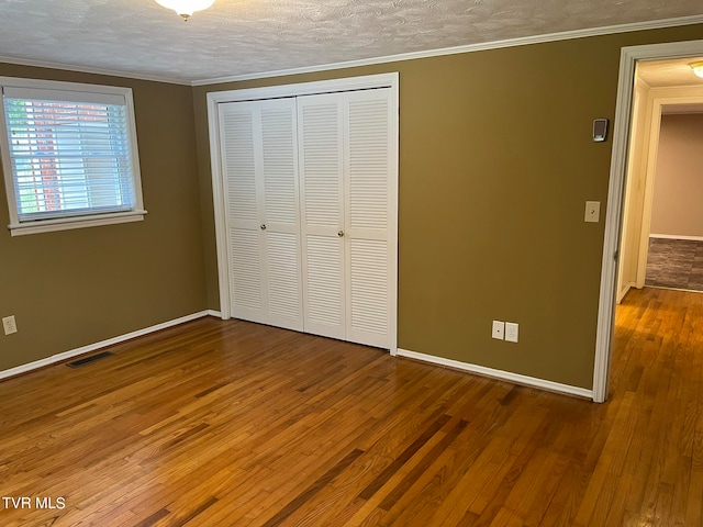 unfurnished bedroom with ornamental molding, a closet, and hardwood / wood-style floors