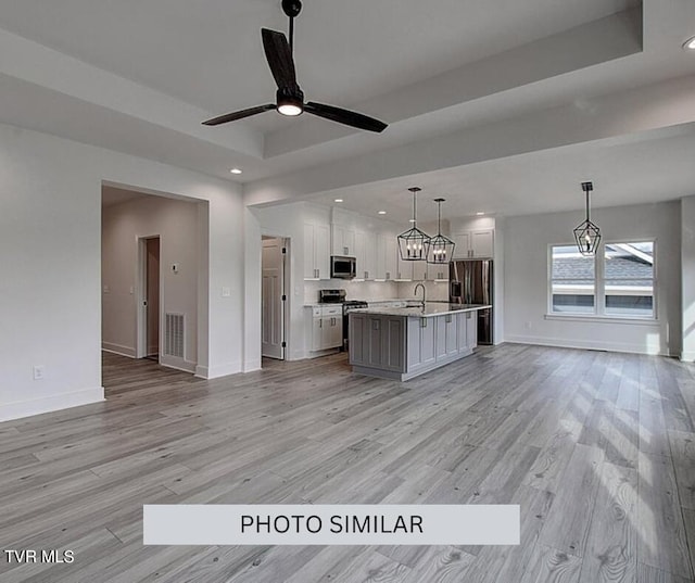 kitchen with ceiling fan with notable chandelier, stainless steel appliances, a center island with sink, light wood-type flooring, and pendant lighting