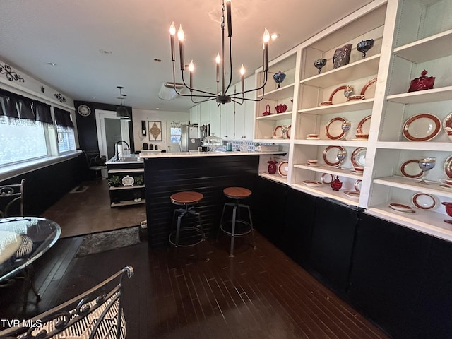 kitchen featuring dark wood-type flooring, a breakfast bar, hanging light fixtures, stainless steel refrigerator, and a notable chandelier