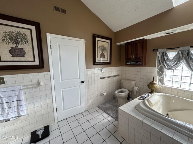 bathroom with tile patterned flooring, tiled bath, a textured ceiling, vaulted ceiling, and toilet