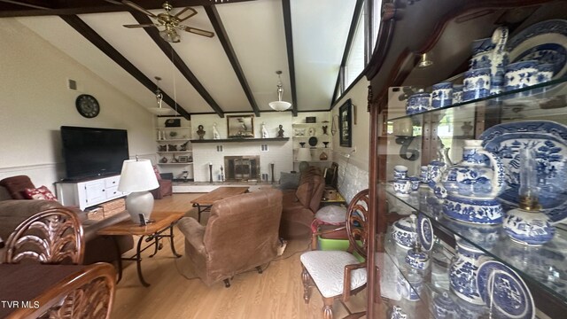 living room featuring a brick fireplace, vaulted ceiling with beams, light hardwood / wood-style floors, and ceiling fan