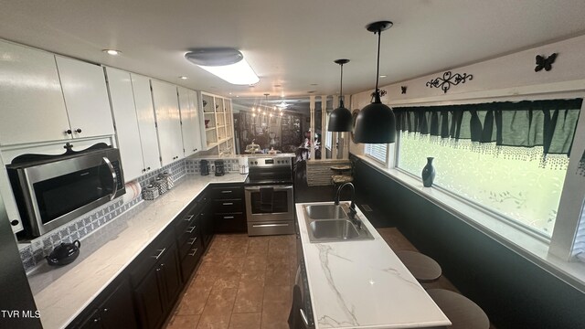 kitchen featuring pendant lighting, sink, white cabinetry, stainless steel appliances, and light stone countertops