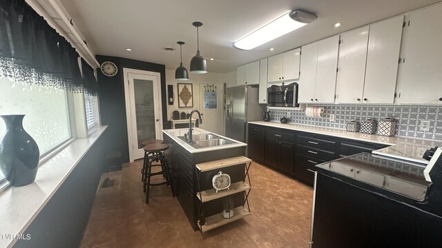 kitchen with sink, appliances with stainless steel finishes, an island with sink, pendant lighting, and white cabinets