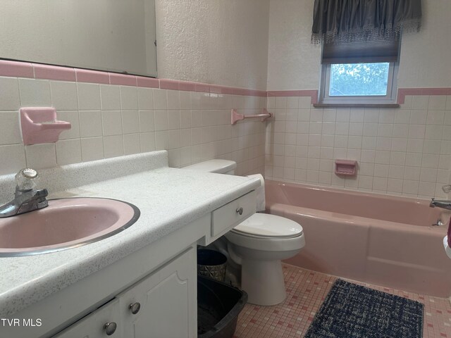 bathroom featuring tile walls, a bathing tub, vanity, tile patterned floors, and toilet