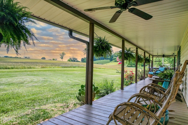 deck at dusk with ceiling fan, a rural view, and a lawn