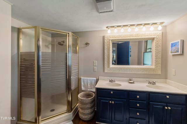 bathroom featuring dual sinks, a shower with shower door, ornamental molding, large vanity, and a textured ceiling