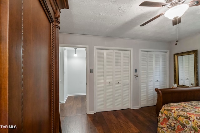 bedroom with a textured ceiling, two closets, ceiling fan, and dark hardwood / wood-style floors