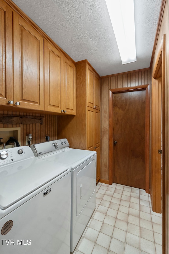 laundry area featuring separate washer and dryer, a textured ceiling, cabinets, wood walls, and light tile floors