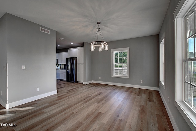 unfurnished dining area featuring a wealth of natural light, light hardwood / wood-style floors, and a notable chandelier