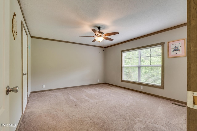 spare room featuring light carpet, ornamental molding, ceiling fan, and a textured ceiling