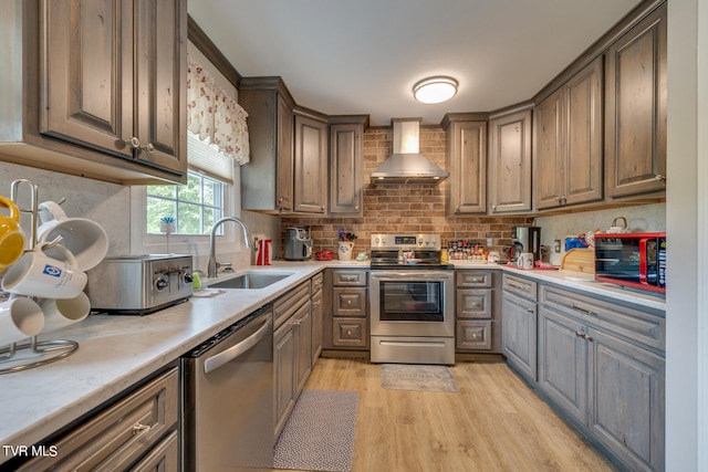 kitchen with tasteful backsplash, wall chimney exhaust hood, light wood-type flooring, appliances with stainless steel finishes, and sink