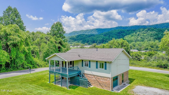 rear view of property featuring a garage, a deck with mountain view, and a lawn