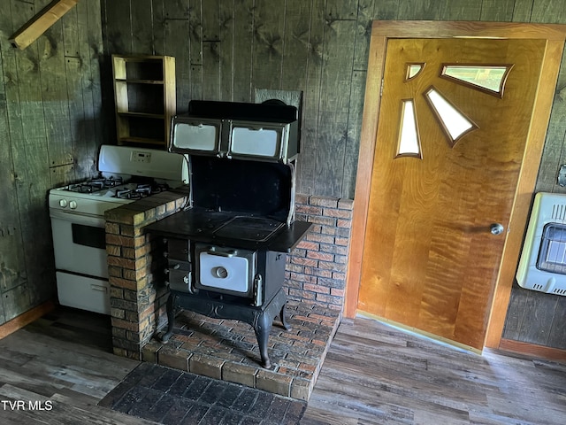 kitchen featuring heating unit, a wood stove, wooden walls, hardwood / wood-style floors, and white gas range oven