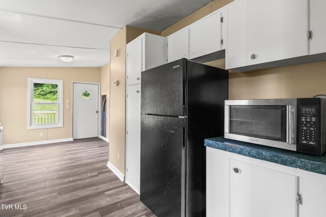 kitchen with black refrigerator, hardwood / wood-style floors, white cabinetry, and vaulted ceiling