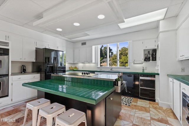 kitchen with white cabinetry, a kitchen island, tile counters, black appliances, and light tile flooring