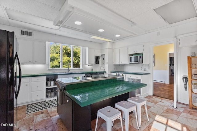 kitchen featuring black appliances, white cabinetry, a kitchen island, and light tile floors