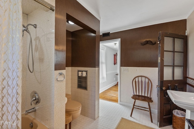 bathroom featuring tile walls, toilet, tile floors, tiled shower / bath combo, and ornamental molding