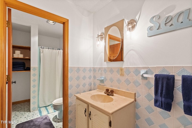 bathroom with tile floors, vanity, toilet, and tile walls