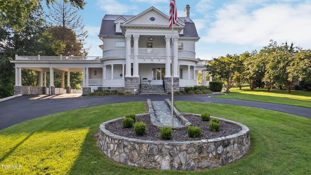 greek revival house with a front yard, a balcony, and a porch