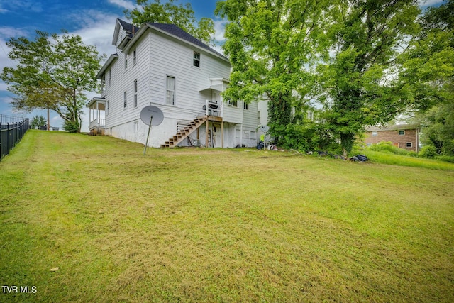 rear view of house with stairway, fence, and a lawn