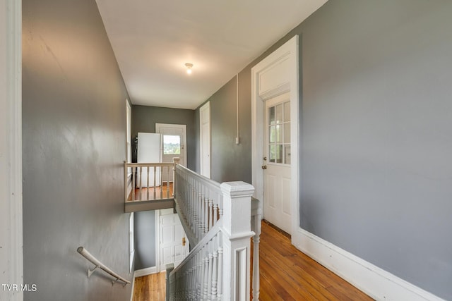 corridor featuring an upstairs landing, baseboards, and wood finished floors