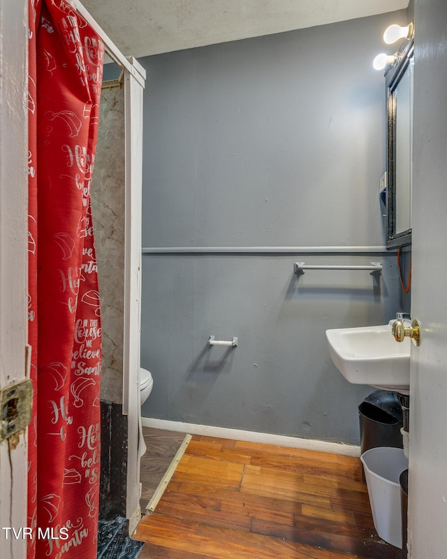 full bathroom featuring baseboards, walk in shower, a sink, toilet, and wood finished floors