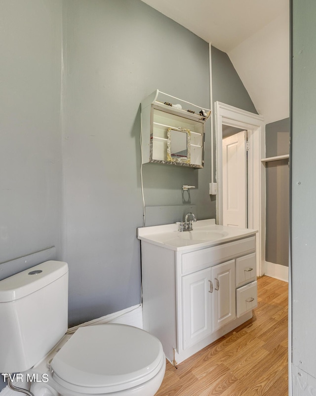 bathroom featuring toilet, wood finished floors, vanity, and vaulted ceiling