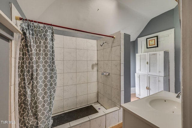 full bath featuring a tile shower, vanity, baseboards, and vaulted ceiling
