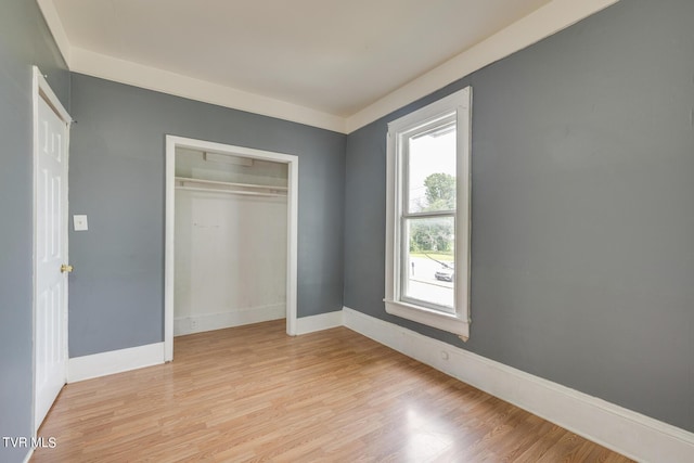 unfurnished bedroom featuring a closet, light wood-type flooring, multiple windows, and baseboards