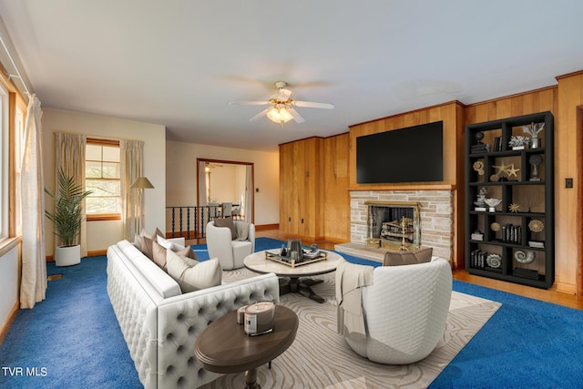 carpeted living room with a stone fireplace, ceiling fan, and wood walls