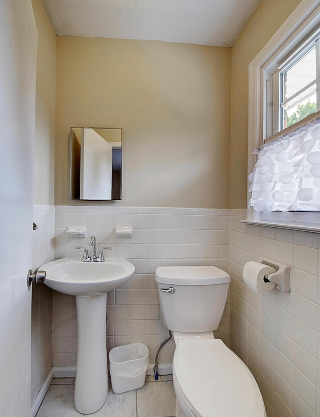 bathroom featuring toilet, a textured ceiling, and tile walls