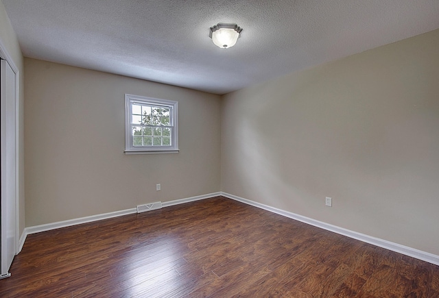 unfurnished room featuring dark wood-type flooring and a textured ceiling