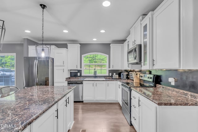 kitchen featuring crown molding, stainless steel appliances, dark stone countertops, hanging light fixtures, and sink