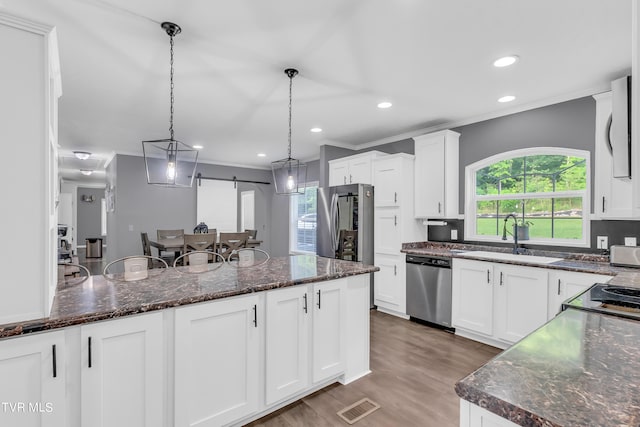 kitchen with stainless steel appliances, pendant lighting, dark stone countertops, sink, and hardwood / wood-style flooring