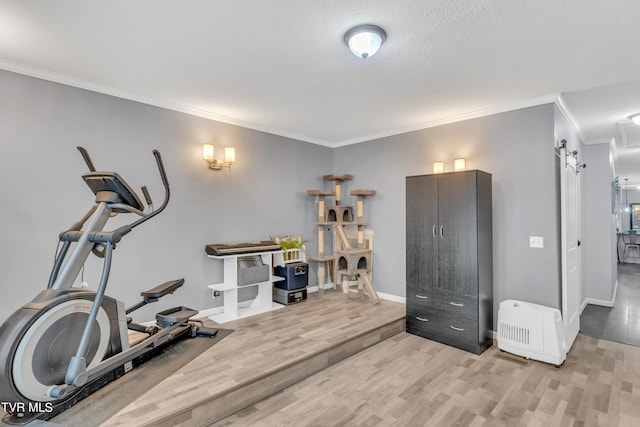 workout room featuring a barn door, light hardwood / wood-style floors, a textured ceiling, and crown molding