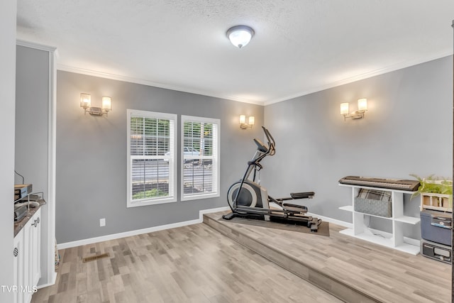 exercise area featuring ornamental molding, a textured ceiling, and light wood-type flooring