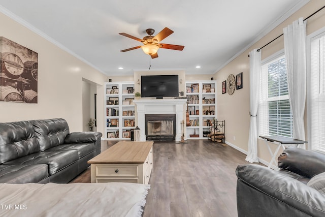 living room featuring ceiling fan, built in shelves, crown molding, and dark wood-type flooring