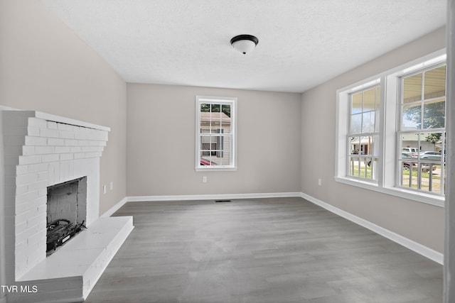 unfurnished living room featuring a healthy amount of sunlight, dark wood-type flooring, and a brick fireplace