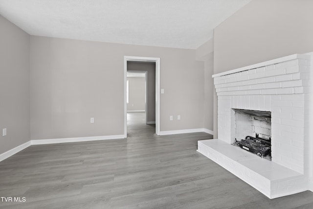 unfurnished living room with hardwood / wood-style flooring, a brick fireplace, and a textured ceiling