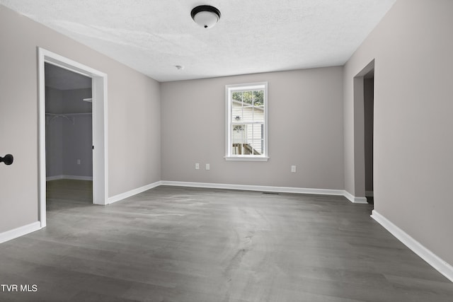 unfurnished bedroom with a closet, dark hardwood / wood-style flooring, a textured ceiling, and a spacious closet