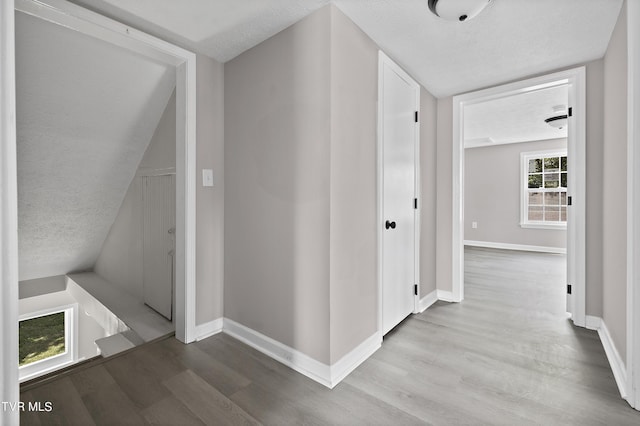 corridor with a textured ceiling and light hardwood / wood-style floors