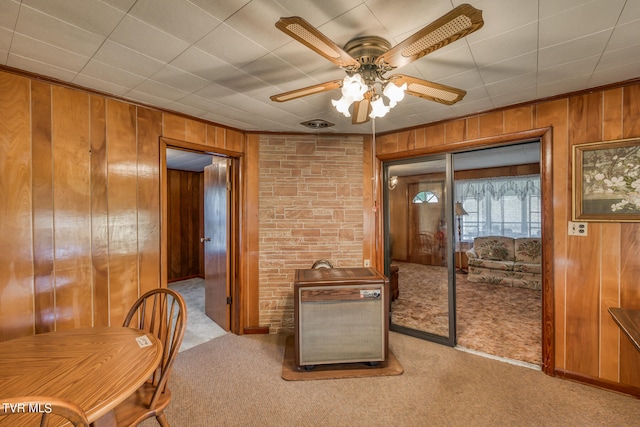 carpeted dining room featuring wood walls and ceiling fan