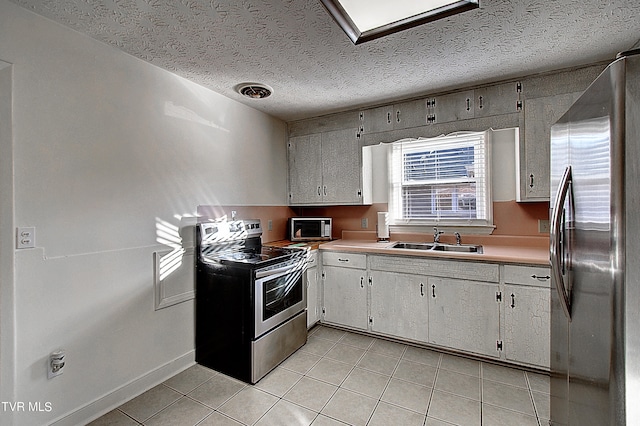 kitchen with light tile patterned floors, a textured ceiling, white cabinets, appliances with stainless steel finishes, and sink