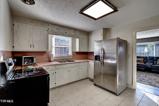 kitchen with stainless steel fridge, range with electric stovetop, a healthy amount of sunlight, and white cabinets