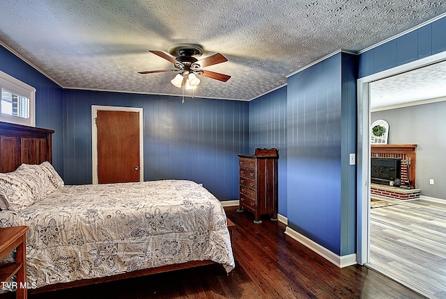 bedroom featuring ceiling fan, ornamental molding, dark hardwood / wood-style floors, a textured ceiling, and a brick fireplace