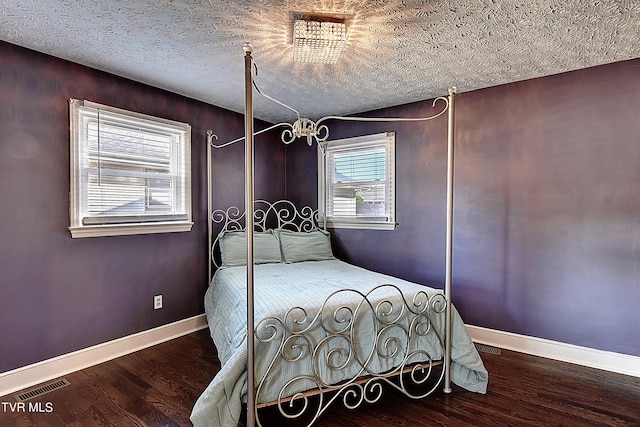 bedroom with multiple windows, a textured ceiling, and dark wood-type flooring