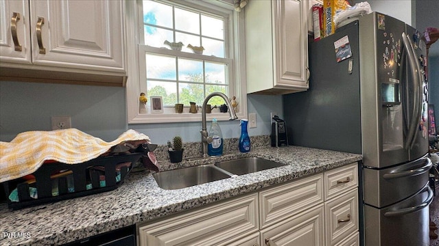 kitchen featuring stainless steel refrigerator with ice dispenser, white cabinetry, sink, and light stone countertops