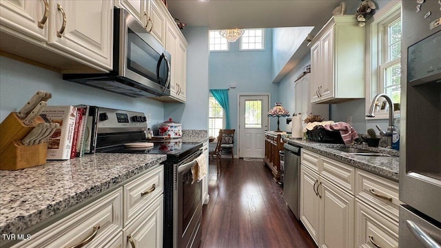 kitchen with dark hardwood / wood-style flooring, appliances with stainless steel finishes, sink, an inviting chandelier, and light stone counters