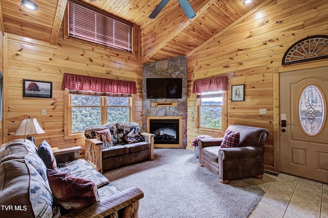 tiled living room with ceiling fan, wooden ceiling, a stone fireplace, high vaulted ceiling, and wood walls