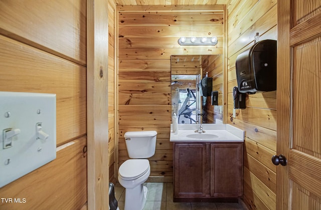 bathroom featuring toilet, vanity, tile patterned floors, and wooden walls